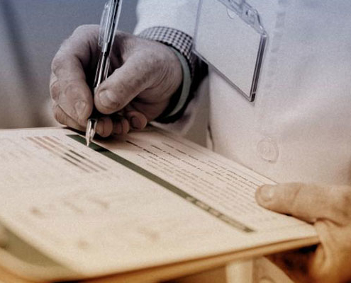 doctor's hands with pen and clipboard writing on a paper form