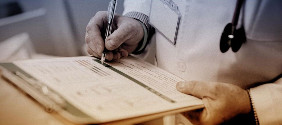 doctor's hands with pen and clipboard writing on a paper form